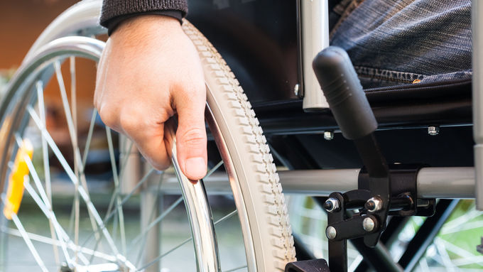 Eine Hand umfasst einen Rollstuhlreifen