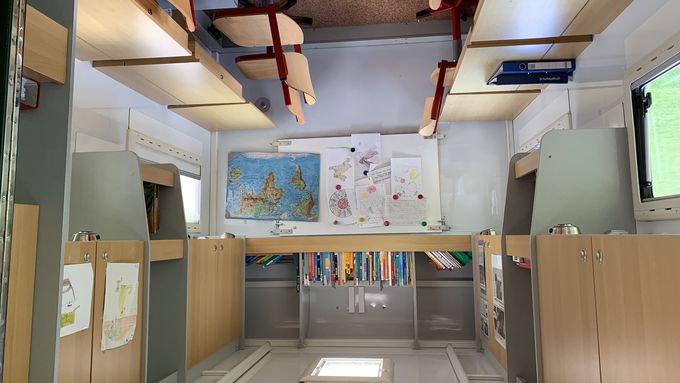 Das Schulmobil von innen: Schulbänke und -tische, Regale und eine Tafel.