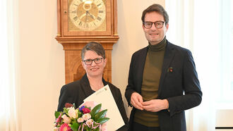 Regierungspräsident Andreas Bothe (l.) überreicht die öffentliche Belobigungsurkunde an Dr. med. Rebekka Falkner (r.).