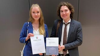 Lea Lamkemeyer und Mike Daßler (Dezernent bei der Bezirksregierung Münster) mit der Urkunde und dem Sammelband "Prämierte Thesisarbeiten"