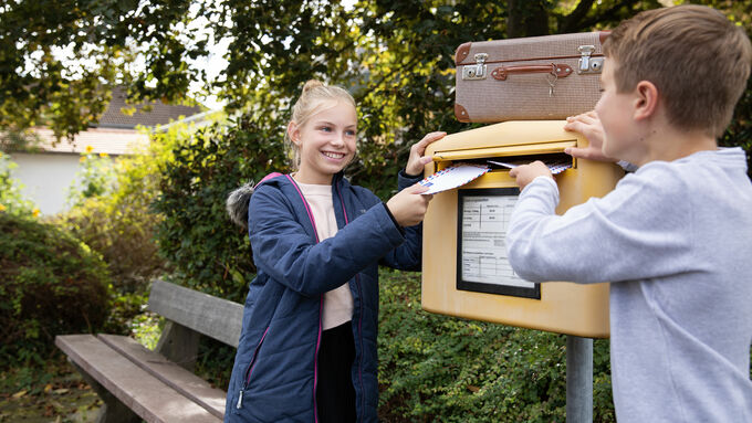 zwei Jugendliche werfen Post in einen Briefkasten
