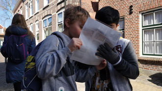 zwei Jungen gucken auf ein Arbeitsblatt, im Hintergrund ein Mädchen