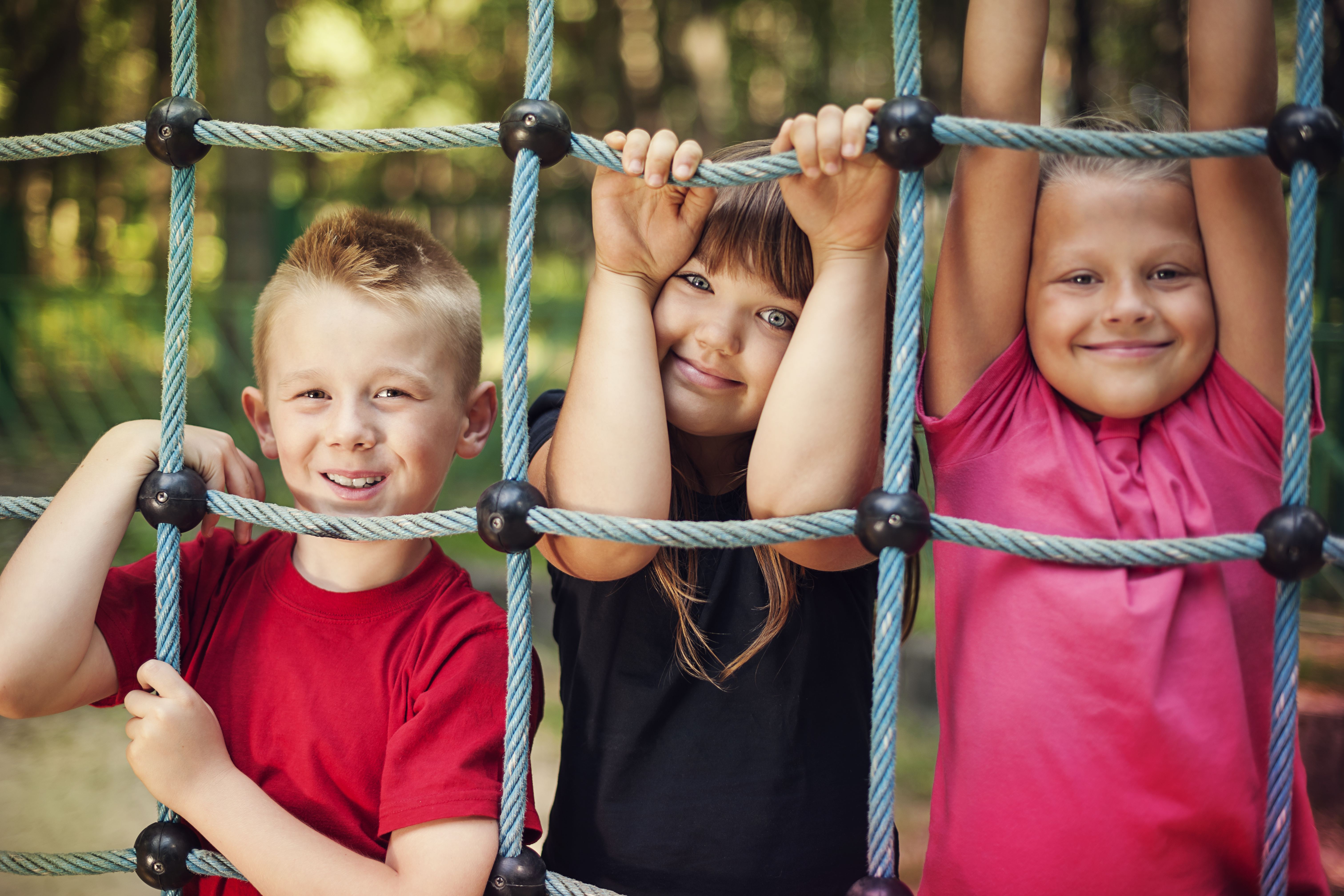 drei Kinder halten stehen hinter einem Spielgerät auf einem Spielplatz