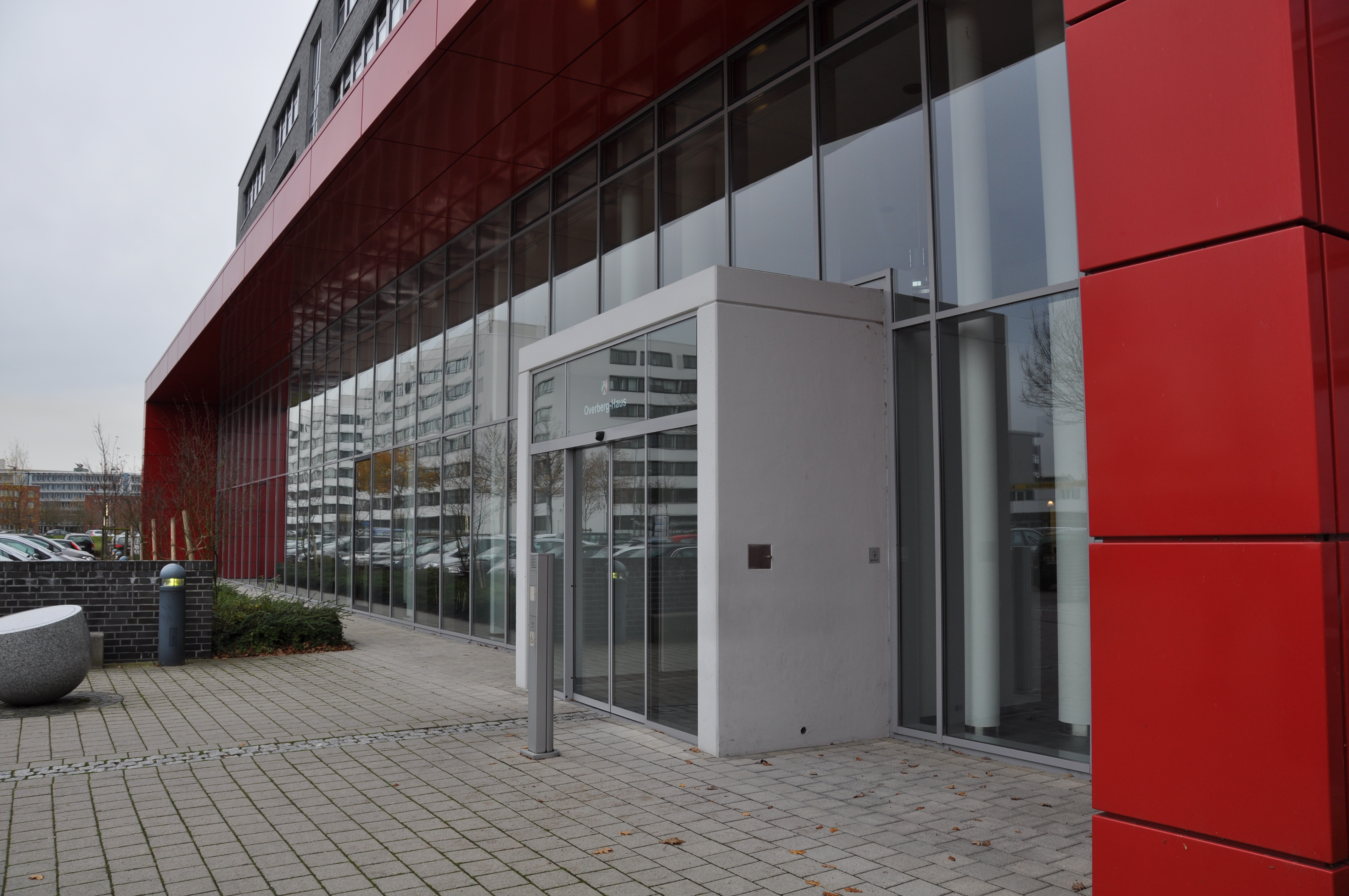 Eingang eines Gebäudes. Die Fassade ist rot und es gibt viele Fenster.