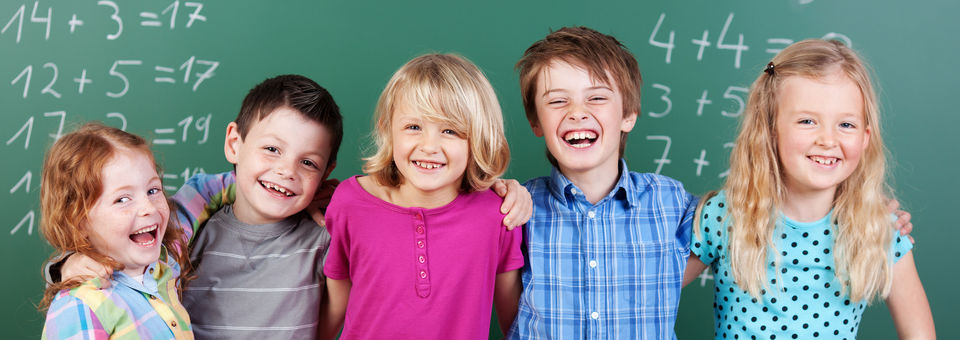 Fünf Kinder lachend vor einer Tafel 