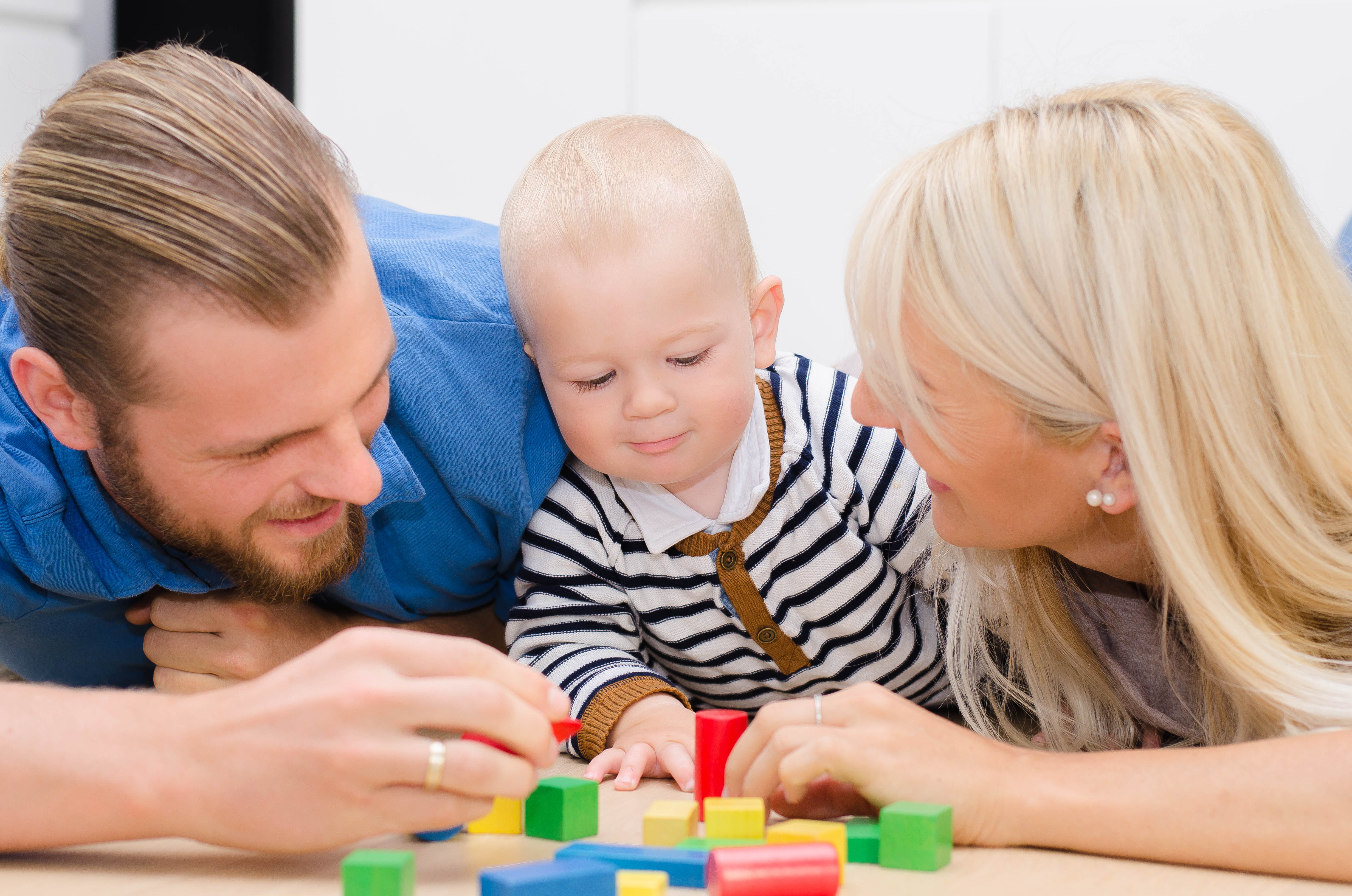Vater, Mutter und kleines Kind spielen auf dem Boden 