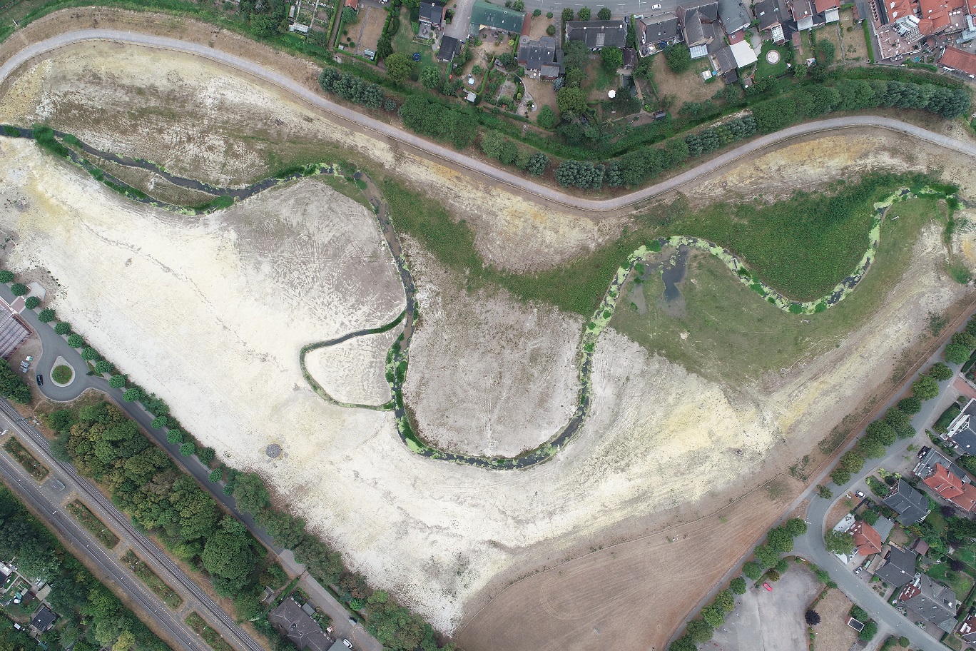 Zu sehen ist die Luftbildaufnahme eines etwa 600 m langen Abschnitts des Emmerbachs, der stark geschwungen durch die gut 7 ha große Deipenwiese am Ortsrand von Ascheberg verläuft. Angrenzend an die Deipenwiese ist der Rundweg zu erkennen, der die gesamte Fläche einschließt. Im oberen und rechten Bildbereich beginnt die Wohnbebauung von Ascheberg. Zwischen der Wohnbebauung und dem Rundweg ist im oberen Bildbereich der Altverlauf des Emmerbachs zu erkennen, der zum Rückhalt von Hochwasser erhalten geblieben i