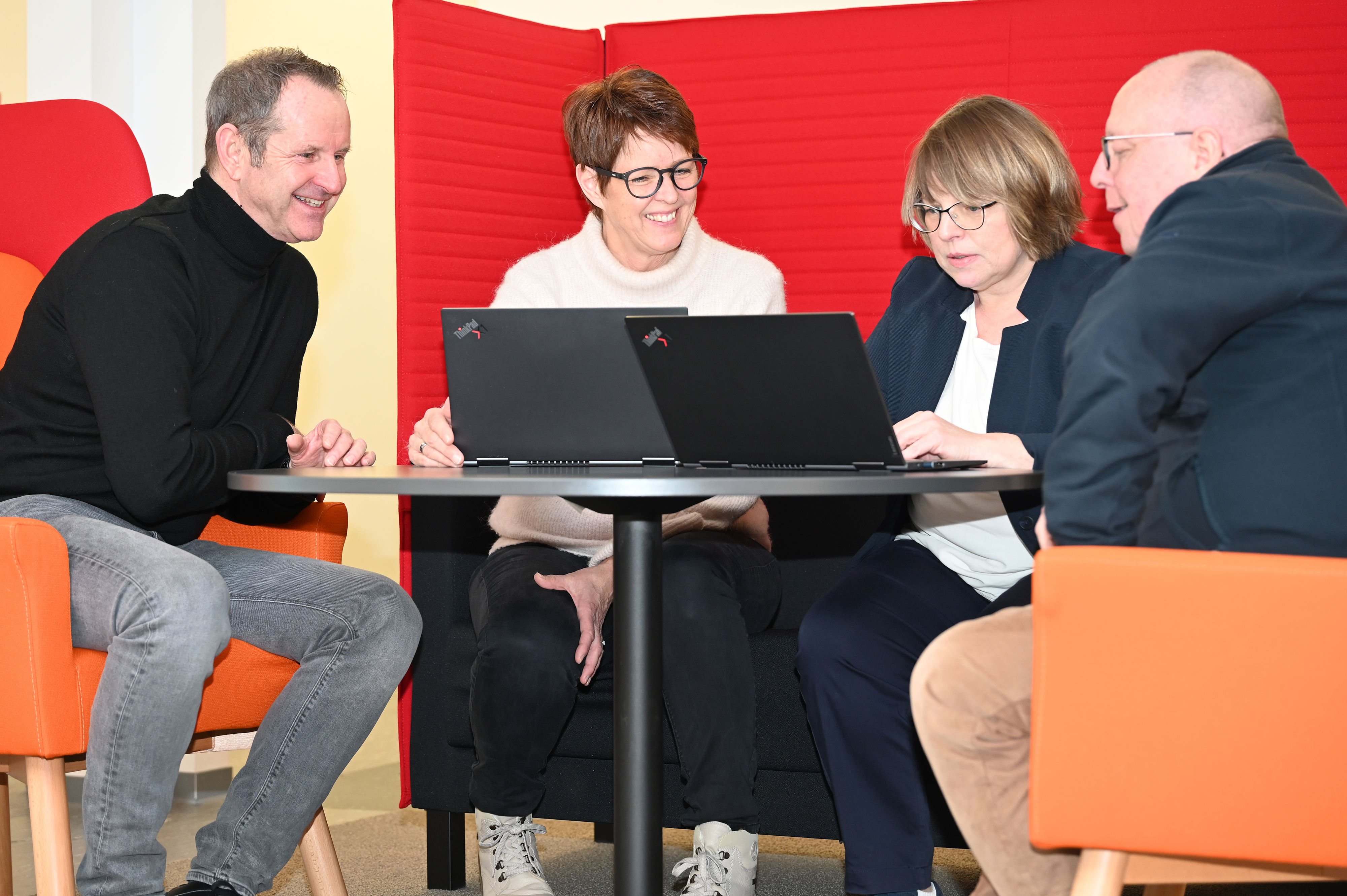 Eine Gruppe von vier Personen sitzt mit Laptops an einem Tisch