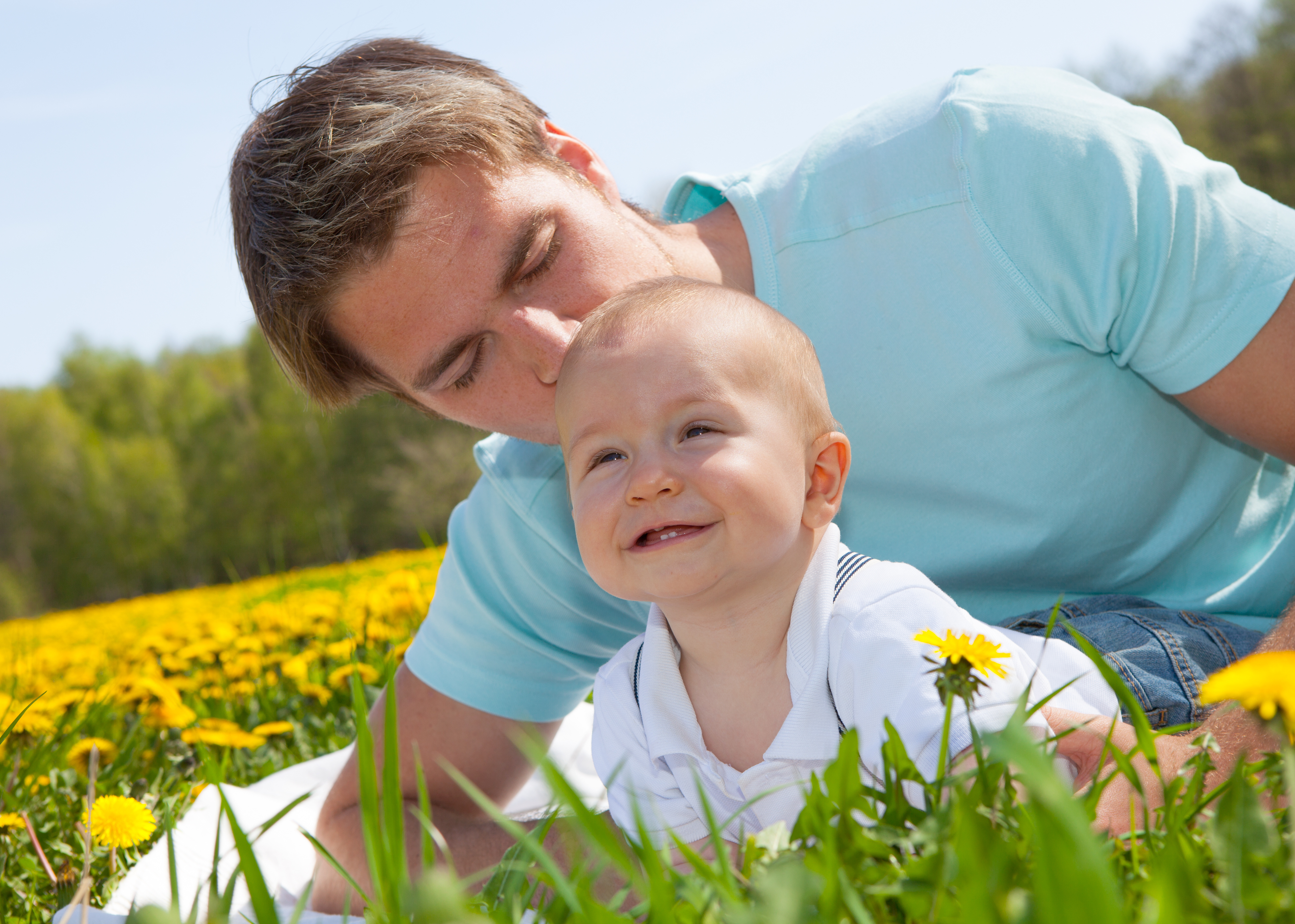 Ein Vater liegt mit seinem Kind auf einem Löwenzahnfeld