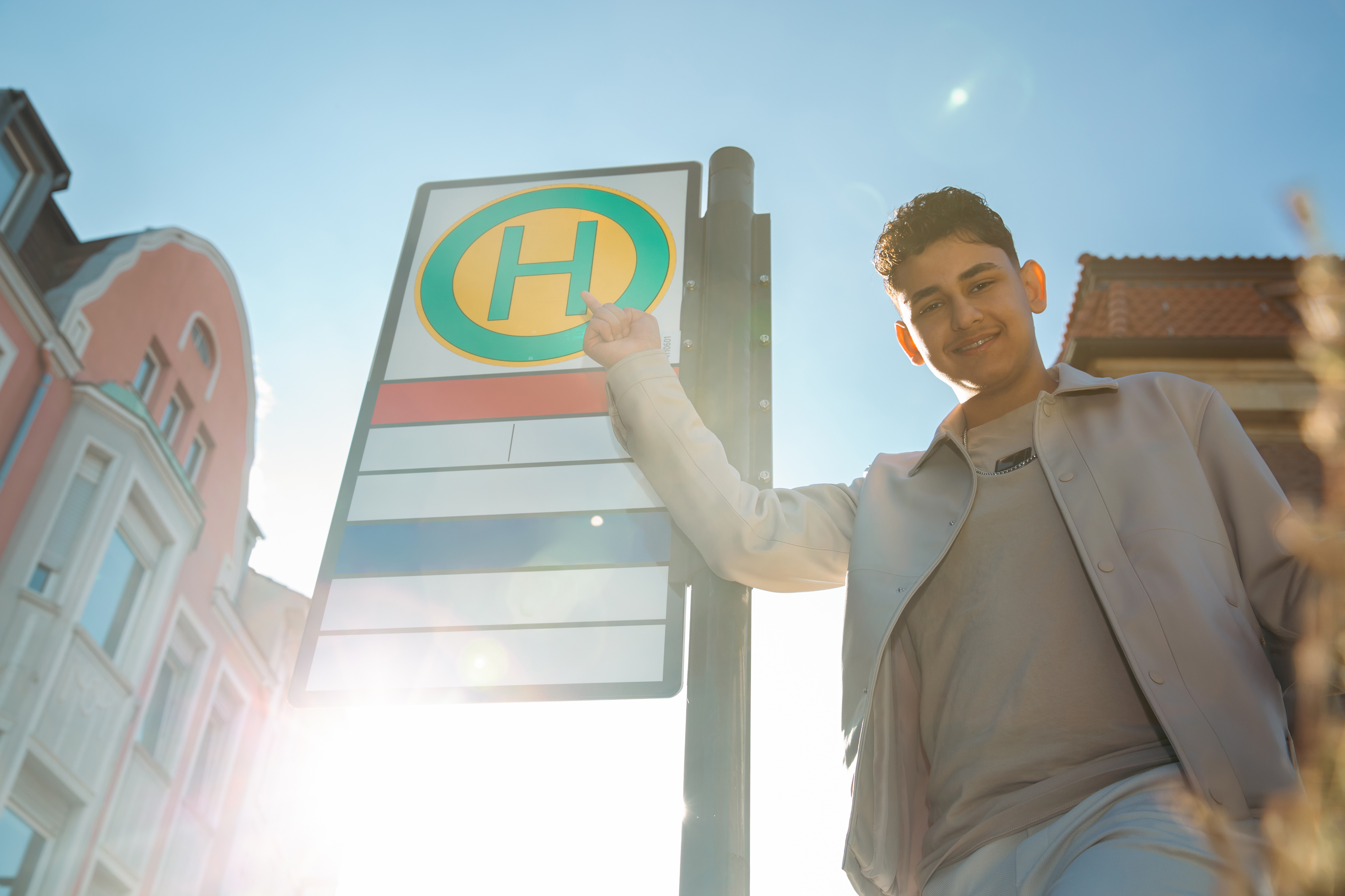 Ein Jugendlicher zeigt auf ein Bushaltestellenschild