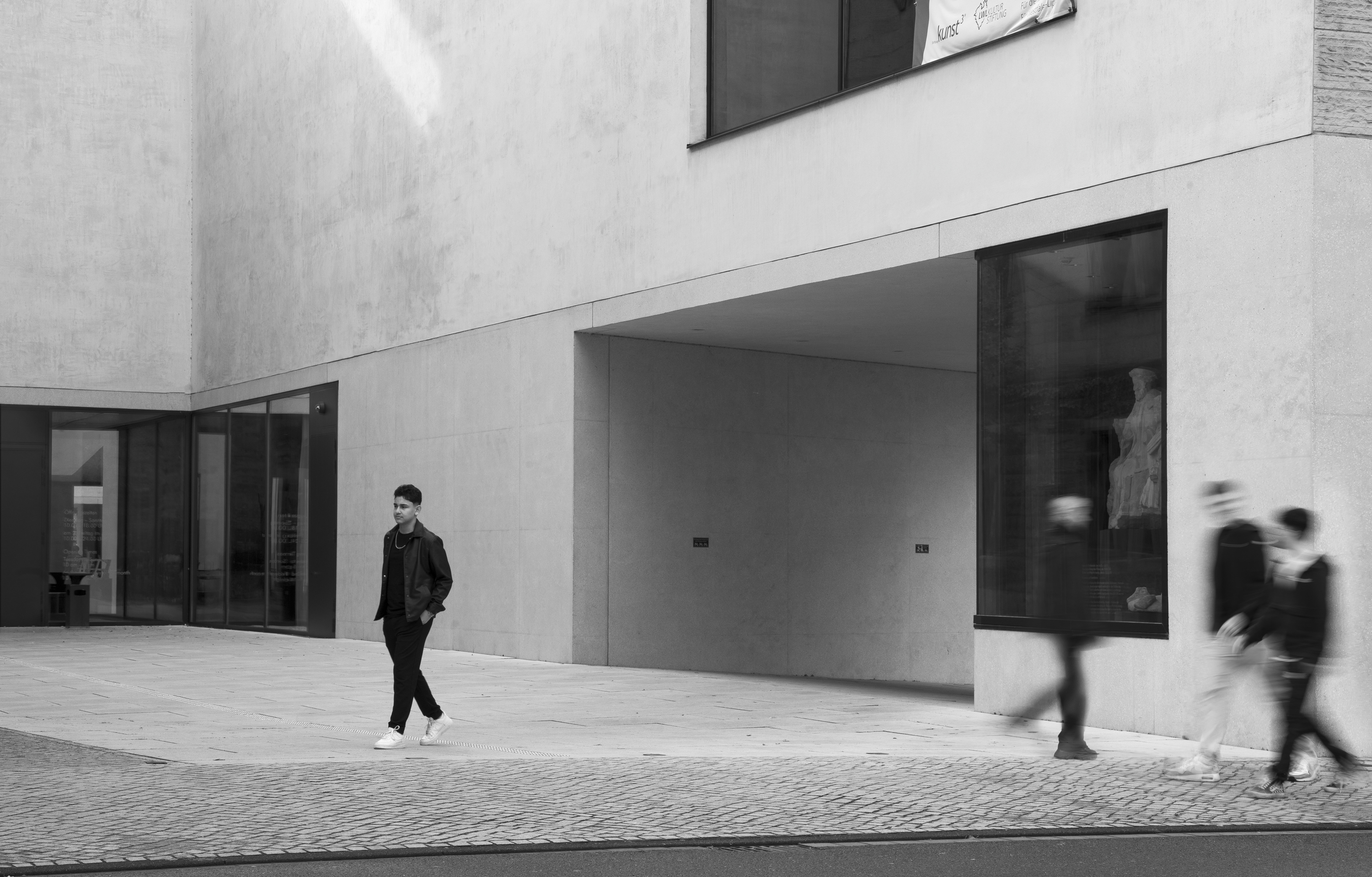 Ein schwarz-weißes Bild auf dem vier Menschen an einem Gebäude lang laufen.