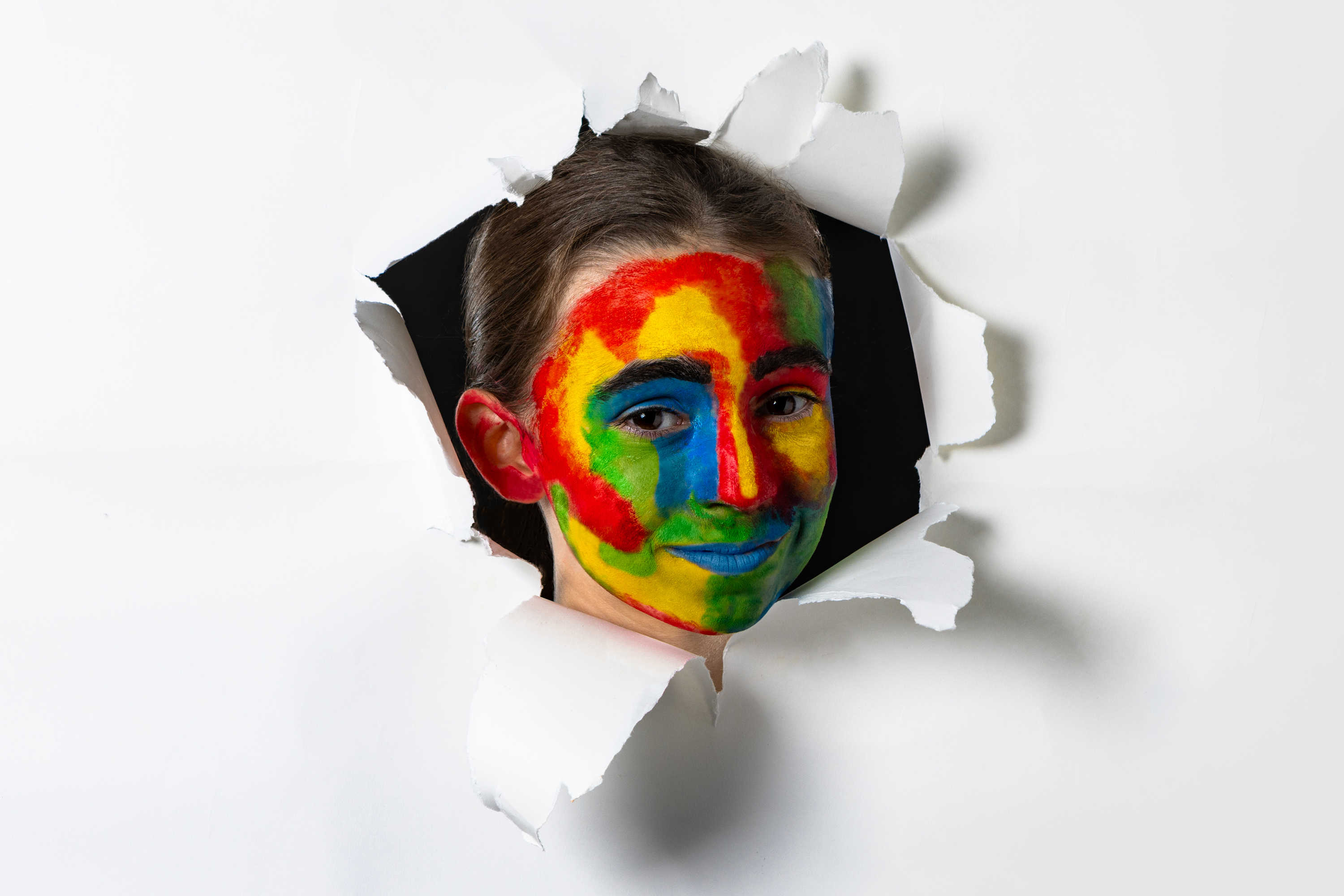 Ein Mädchen mit einem bunt bemalten Gesicht schaut durch ein Loch in einer Leinwand.