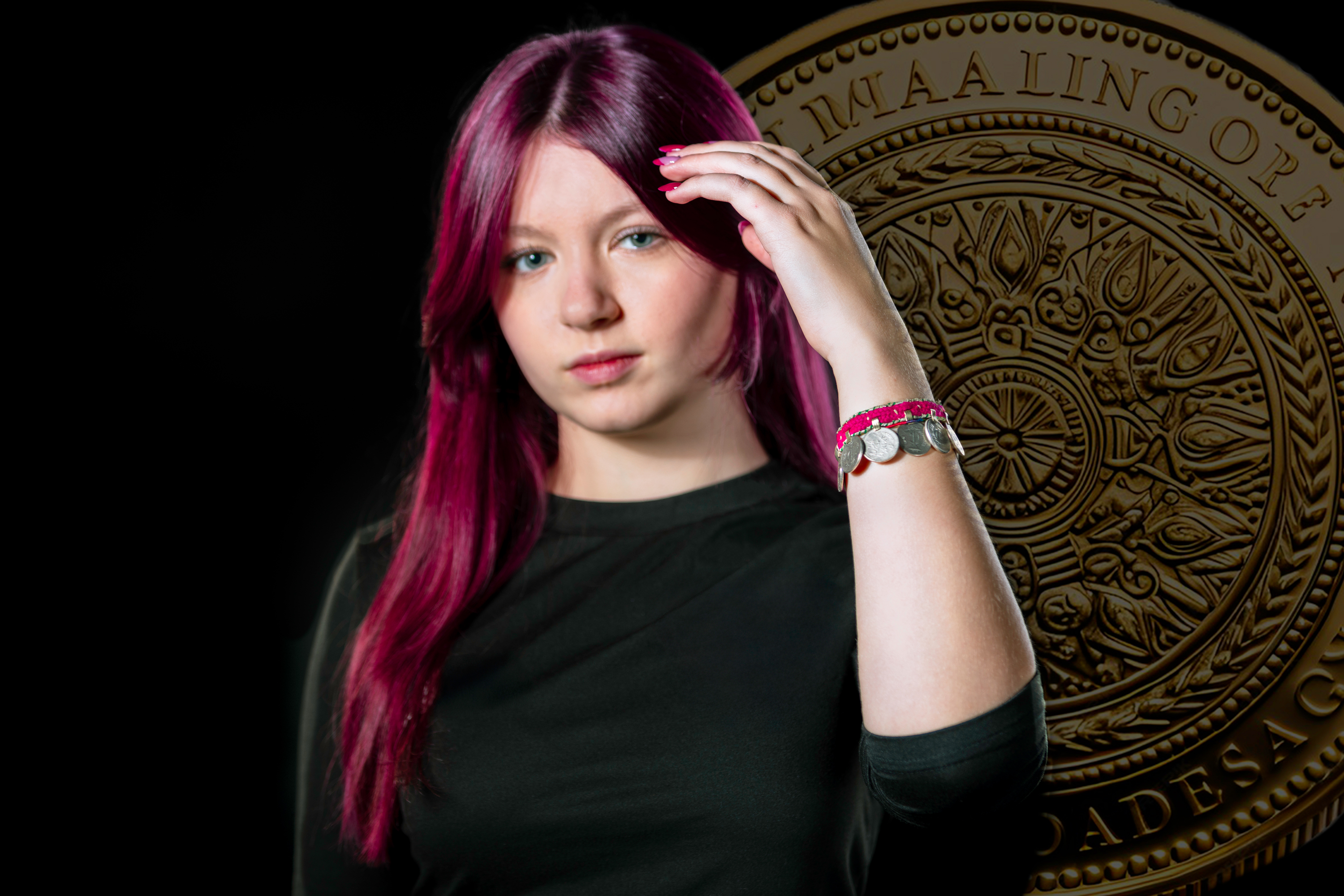 Eine weibliche Jugendliche hälte den linken Arm nach vorne. Dort befindet sich ein Armband mit Münzen. Im Hintergrund ist eine große Münze zu sehen.