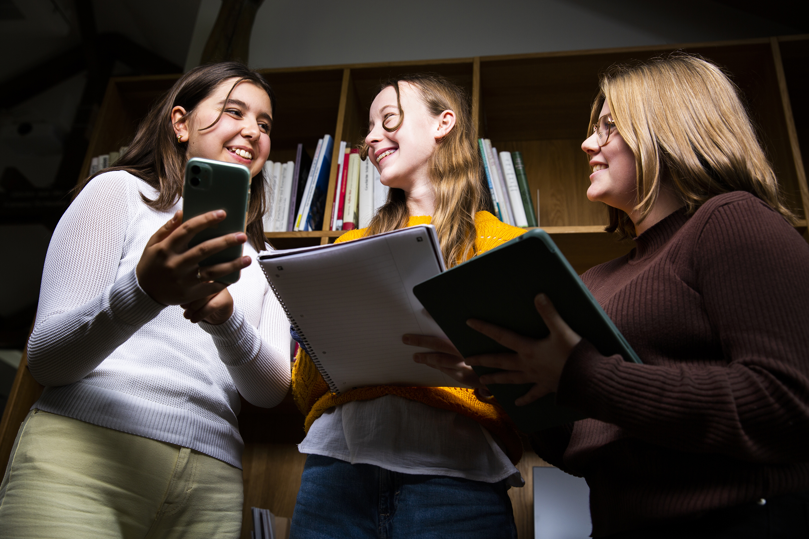 Drei Jugendliche halten Bücher und ein Smartphone