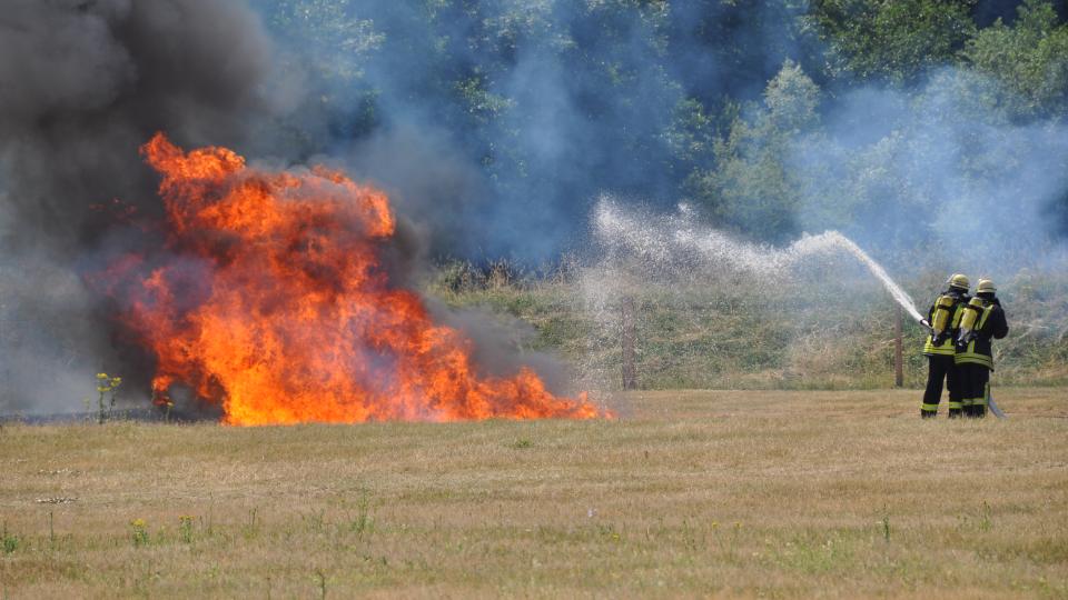 Zwei Feuerwehrmänner löschen einen Brand auf einer Wiese.