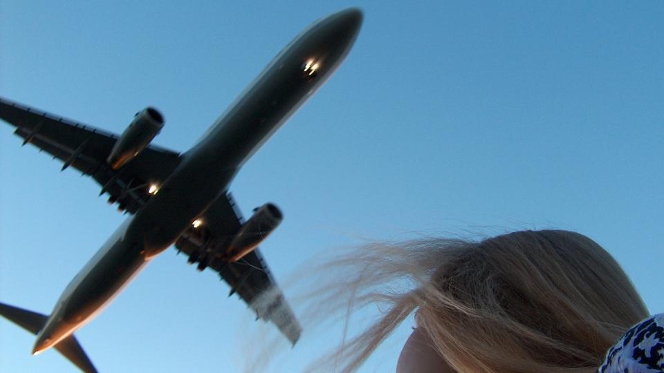 Eine Frau schaut auf ein über ihr fliegendes Flugzeug