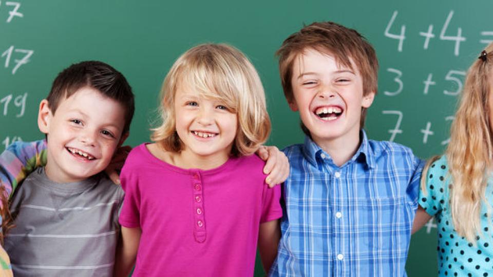 Fünf Kinder lachend vor einer Tafel 