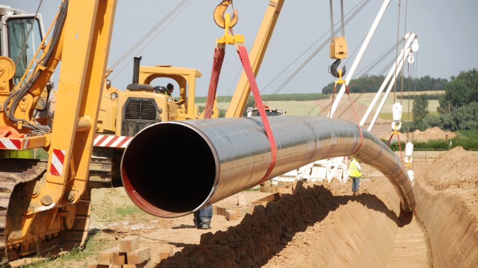 Ein Kran hebt ein Rohr in einen Graben