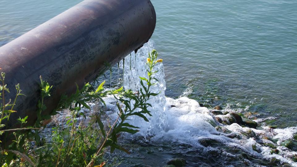 Das Foto zeigt ein wasserführendes Rohr mit ca. 50 cm Durchmesser, das oberhalb einer Gewässeroberfläche endet. Aus dem Rohr fließt Wasser in das Gewässer.