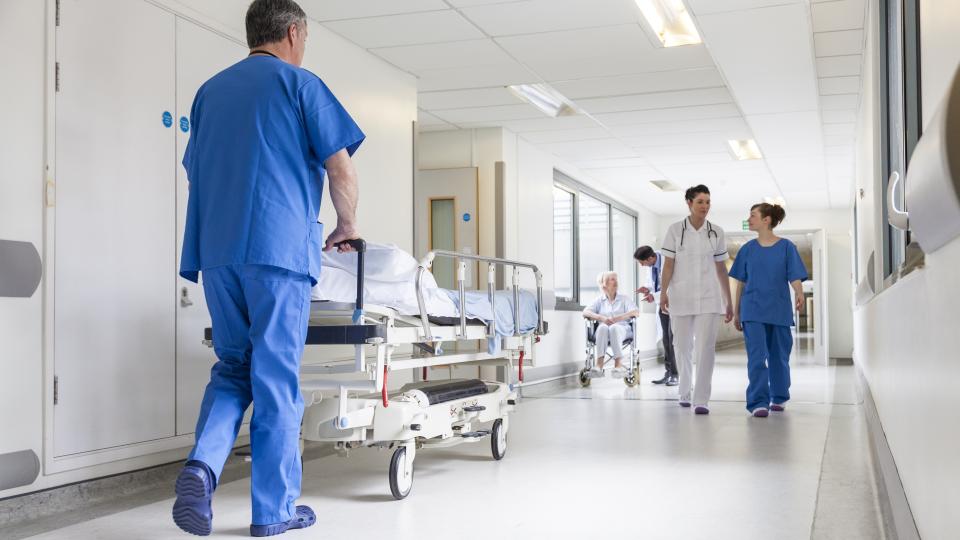Ein Pfleger schiebt ein Bett durch einen Krankenhausflur