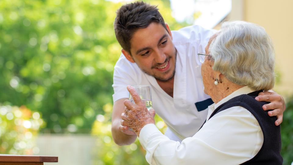 Ein Pfleger beugt sich zu einer älteren Dame herunter