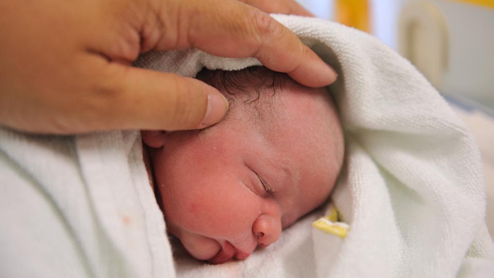 Ein Neugeborenes wird am Kopf gestreichelt