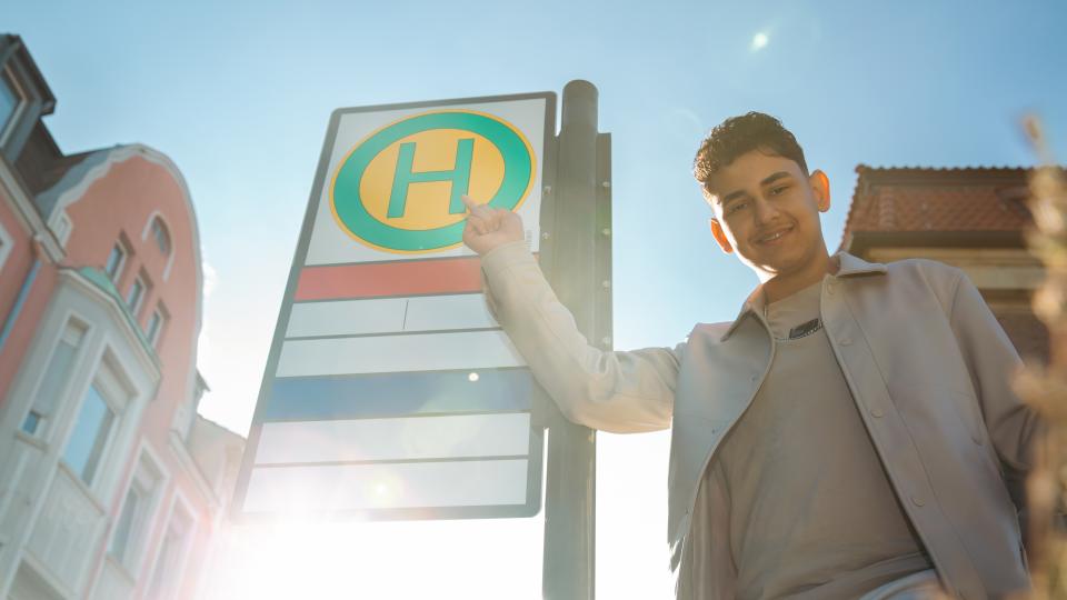 Ein Jugendlicher zeigt auf ein Bushaltestellenschild