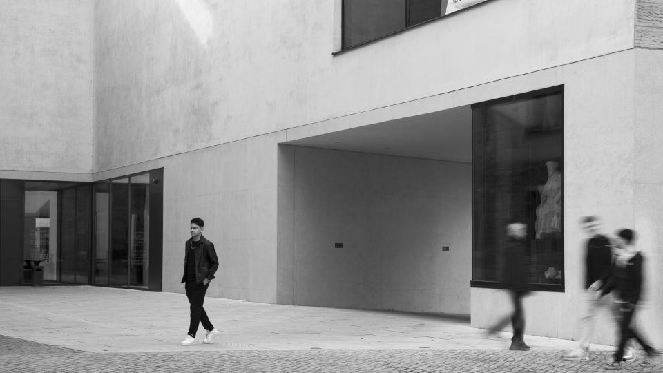 Ein schwarz-weißes Bild auf dem vier Menschen an einem Gebäude lang laufen.