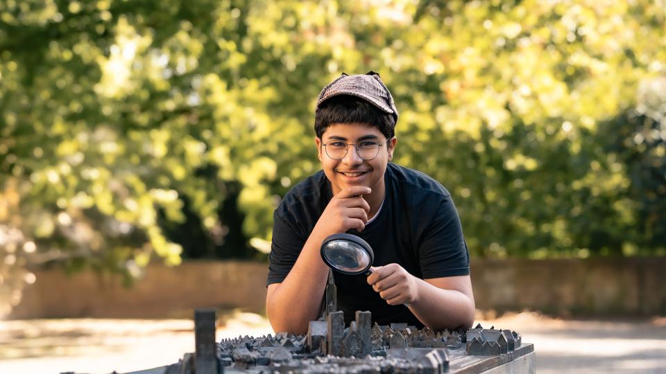 Ein Junge schaut - mit einer Lupe in der Hand - auf ein 3D-Modell von Münster 