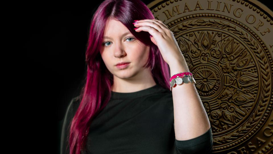 Eine weibliche Jugendliche hälte den linken Arm nach vorne. Dort befindet sich ein Armband mit Münzen. Im Hintergrund ist eine große Münze zu sehen.