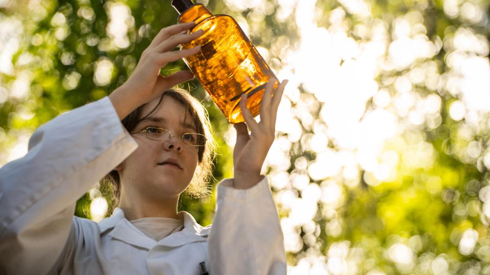Eine weibliche Jugendliche schaut auf ein braunes Apothekenglas.