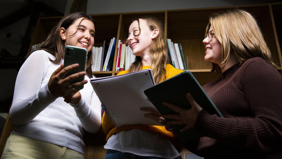 Drei Jugendliche halten Bücher und ein Smartphone