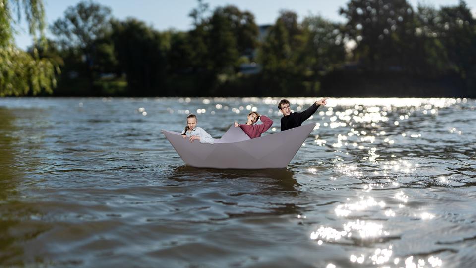 Drei Jugendliche in einem Papierboot