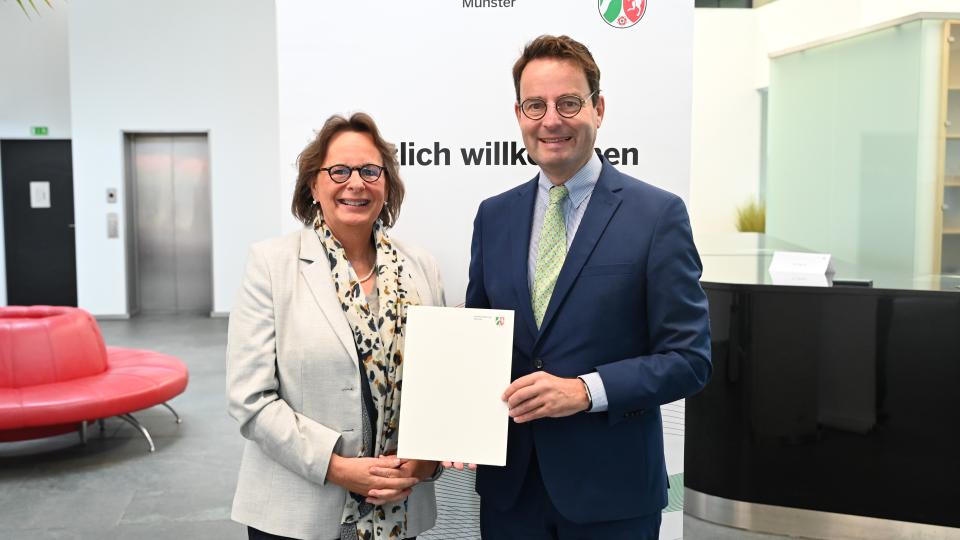 Regierungspräsident Andreas Bothe (r.) übergibt den Förderbescheid für die energetische Sanierung der Dreifachsporthalle Gescher an Bürgermeisterin Anne Kortüm.