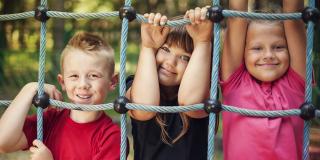 drei Kinder halten stehen hinter einem Spielgerät auf einem Spielplatz
