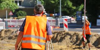 Vermesser mit Warnweste auf Straßenbaustelle