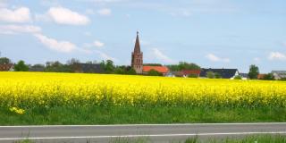 Straße vor Rapsfeld und dörflicher Siedlung mit Kirchturm