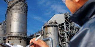 Eine Person mit einem Klemmbrett steht vor einer Industrieanlage