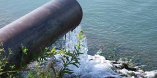 Das Foto zeigt ein wasserführendes Rohr mit ca. 50 cm Durchmesser, das oberhalb einer Gewässeroberfläche endet. Aus dem Rohr fließt Wasser in das Gewässer.