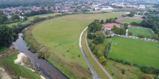 Luftbild mit Blick über die Baufläche vor Beginn der Arbeiten. Im Vordergrund links ist der umgestaltete Mündungsbereich der Münsterschen Aa zu sehen, im Hintergrund die Fußgängerbrücke am Hallenbad in Greven 