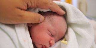 Ein Neugeborenes wird am Kopf gestreichelt