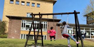 Zwei Mädchen schaukeln vor einer Unterkunft