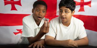 Zwei Jungen schauen auf einen Diamanten, den einer der Jungen in der Hand hält. Im Hintergrund ist die Fahne von Georgien