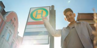 Ein Jugendlicher zeigt auf ein Bushaltestellenschild