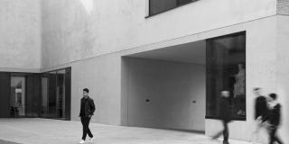 Ein schwarz-weißes Bild auf dem vier Menschen an einem Gebäude lang laufen.