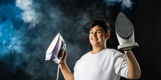 Ein männlicher Jugendlicher hält zwei Dampfbügeleisen hoch. Im Hintergrund ist Dampf und Nebel zu sehen.