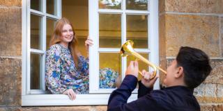 Eine weibliche Jugendliche sitzt in einem Fenster, davor ein männlicher Jugendlicher der Trompete spielt.