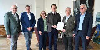 Regierungspräsident Andreas Bothe (4. v. l.) übergibt die Urkunde zur Anerkennung der „Emsdettener Stiftung für Frieden und Völkerverständigung“ an den Stiftungsvorstand.