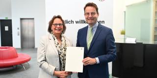 Regierungspräsident Andreas Bothe (r.) übergibt den Förderbescheid für die energetische Sanierung der Dreifachsporthalle Gescher an Bürgermeisterin Anne Kortüm.